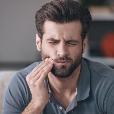 Man in need of emergency dentistry holding cheek in pain