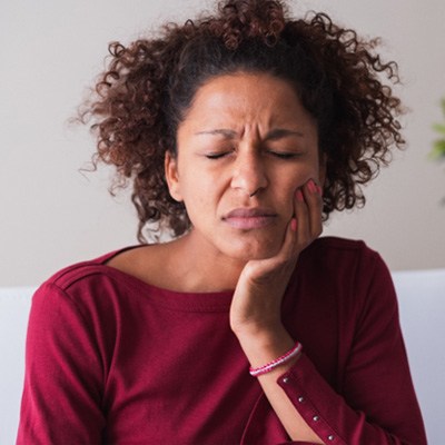 Woman sitting on couch rubbing her jaw in pain