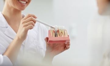 Dentist pointing to model of dental implant replacement tooth compared to natural teeth