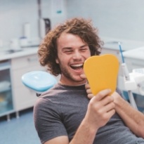 Young man looking at his smile in mirror after Invisalign treatment