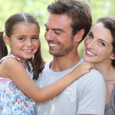 Family of three sharing healthy aligned smile after orthodontic treatment with Invisalign