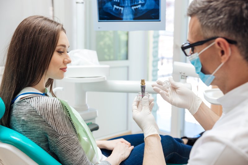 A dentist holding titanium dental implants in front of a patient
