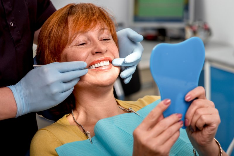 Older woman looking at her implant bridge after tooth loss